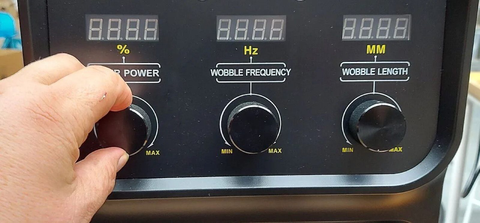 Hand turning the laser power knob on a handheld laser welder control panel with power, wobble frequency and wobble length dials
