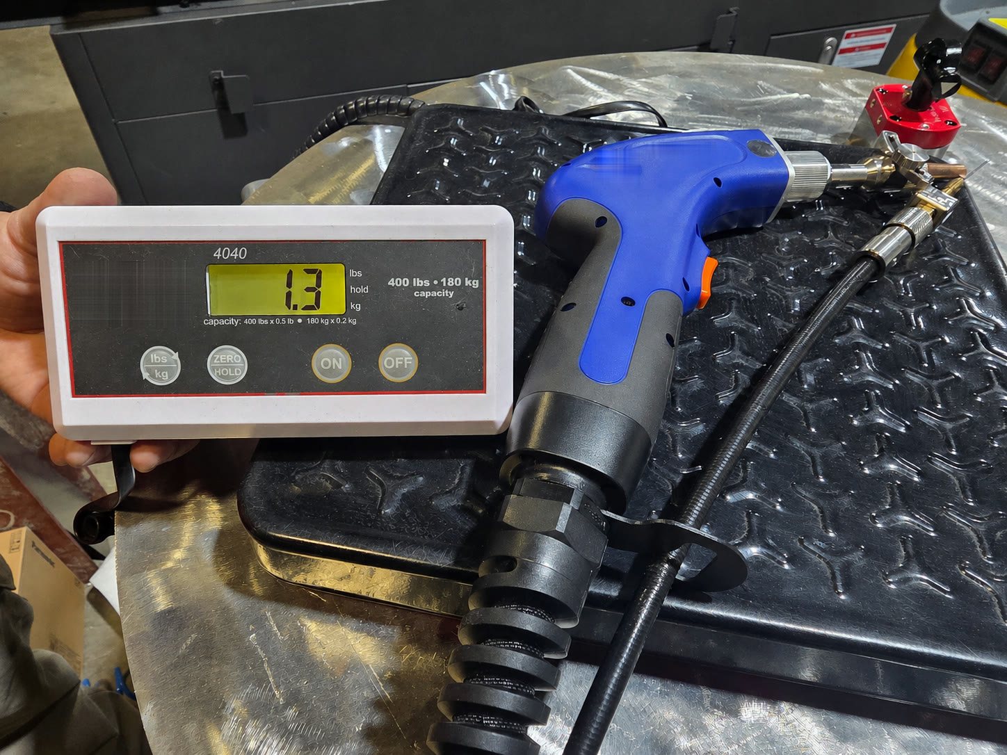 Handheld laser welding torch lying on a shop scale beside the display unit of the scale